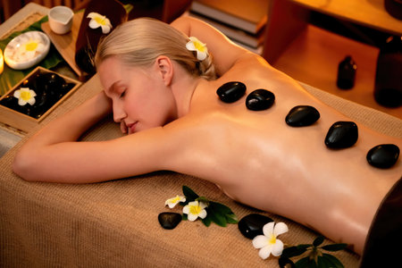 Hot stone massage at spa salon in luxury resort with warm candle light, blissful woman customer enjoying spa basalt stone massage glide over body with soothing warmth. Quiescentの写真素材