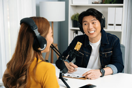 Smiling radio influencer host wearing headphone interviewing woman speaker sharing information to listeners on social media online website live streaming channel at morning at studio record. Infobahn.の写真素材