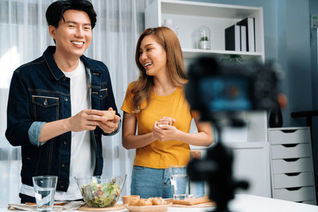 Cooking show on live streaming with two chef influencers teaching mixed salad, preparing ingredients with dressing for easy special menu served with bun bread on table recorded by camera. Infobahn.の写真素材