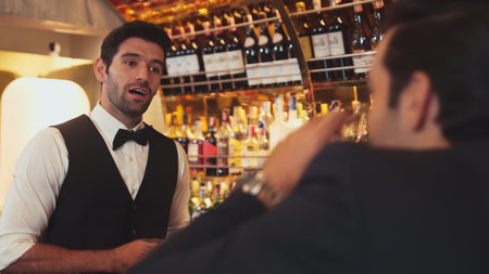 Focusing on smiling smart bartender preparing drinks at luxurious bar while engaging lively conversation with VIP customer at vibrant warm lighting atmosphere bottle bar and pub background. Vinosity.の写真素材