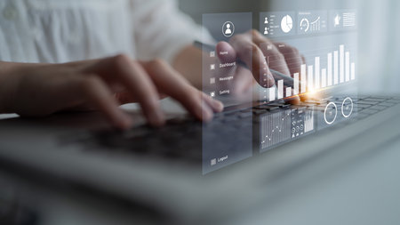 Close-up view of hands typing on a laptop with digital graphs and analytics on the screen, showcasing modern business performance and data analysis. Imputeの写真素材