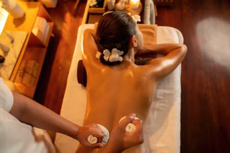 Top view hot herbal ball spa massage body treatment, masseur gently compress herb bag on woman body. Tranquil and serenity of aromatherapy recreation in warm lighting of candle at spa salon. Quiescentの写真素材
