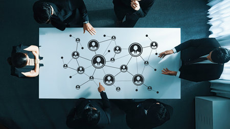 A team of business professionals collaborates around a networking table featuring digital icons,...