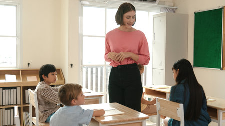 Caucasian teacher walking and check student homework at classroom while diverse children doing classwork at classroom. Diverse smart student lecturing and taking a note at elementary school. Pedagogy.の写真素材