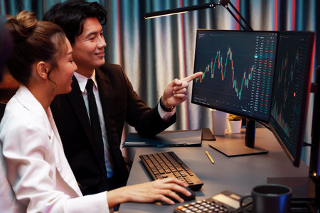 Smiling Asian business traders pointing to dynamic stock exchange data screen profit value online...