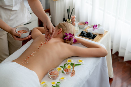 Woman customer having exfoliation treatment in luxury spa salon with warmth candle light ambient. Salt scrub beauty treatment in health spa body scrub. Quiescentの写真素材