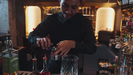Portrait of a good-looking Asian bartender using a jigger to measure liquor into a mixing glass at a...