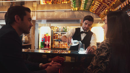 Focusing smiling smart bartender serving gin fizz or tonic soda at luxurious bar, engaging lively...
