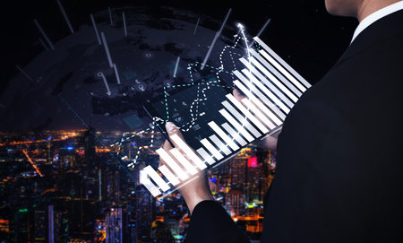 A businessman analyzes financial data through digital graphs, showcasing insights against a stunning night city skyline, representing modern business success. Imputeのeditorial素材