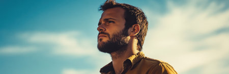 A thoughtful man stands outdoors, gazing into the distance under a clear blue sky. His serious expression reflects contemplation and a sense of adventure.の素材