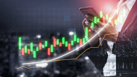 A businessman examines stock market trends using a smartphone. Financial graphs overlay an urban...