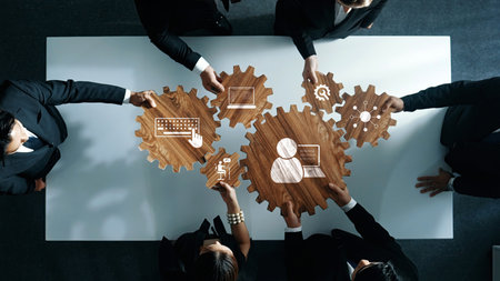 A captivating overhead view of diverse professionals collaborating around a table, using wooden gears and icons to symbolize technology and teamwork in a modern business environment.の写真素材