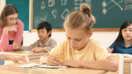 Stressful student focus on doing test while sitting in front of blackboard while multicultural children writing or answering question at classroom. Skilled teacher explain about classwork. Pedagogy.の写真素材