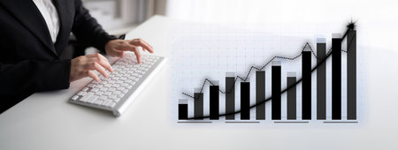 A business professional works at a keyboard while analyzing a graphical display of financial data...