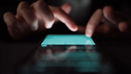 A close-up view captures hands interacting with a smartphone screen in a dimly lit setting, highlighting modern communication and technology usage in daily routines.の写真素材