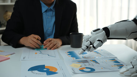 A modern business meeting featuring a human and a robot discussing financial data. The collaborative atmosphere emphasizes technology's role in data analysis and decision-making.の写真素材