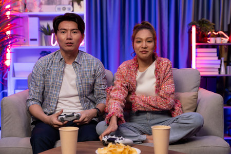 Sitting sofa of happy couple playing video game with joysticks, smiling man playing challenge,...