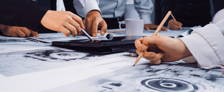 Hands engaged in a discussion over graphical design plans and technical drawings during a...