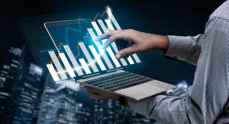 A professional in business attire interacts with a laptop displaying digital graphs and charts,...