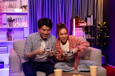 Sitting sofa of happy smiling couple playing video game control by joystick fronted snack and drinks...