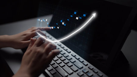 A close-up view of hands typing on a keyboard with a digital graph displaying an upward trend on the...