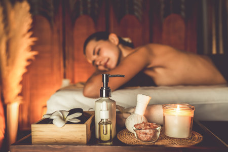 Aromatherapy massage ambiance or spa salon composition setup with focus decor candles and spa accessories on blurred woman enjoying blissful aroma spa massage in resort or hotel background. Quiescentの写真素材