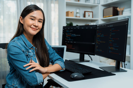 Young Asian in IT developer looking at camera to present with online information on pc with coding program data application, wearing jeans shirt. surround by safety analysis two screens. Stratagem.の写真素材