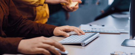 A detailed close-up view of creative professionals working together in a bright office space, showcasing their hands on a keyboard and colorful sticky notes.の写真素材