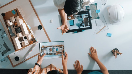 Top view of civil engineer team looking at a tablet and planning building design. Architect looking at project plan while presenting to an investor at a meeting table with blueprint and house model.の写真素材
