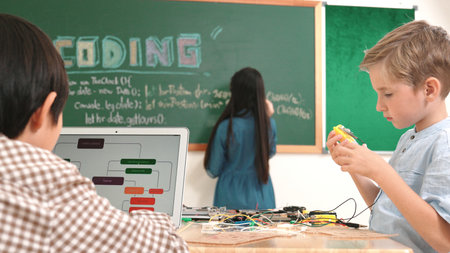 Asian boy coding program while caucasian friend fixing electric board at STEM class. Energetic...