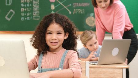 Girl coding prompt while looking at camera at STEM class while teacher checking boy software...