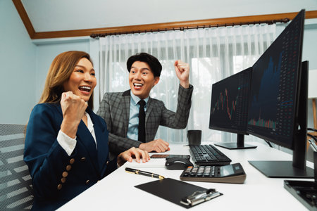 Successful smiling Asian business partners raising fist up together in profitable project job in...