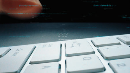 Close-up view of a laptop keyboard with hands typing amidst floating digital codes. This image...