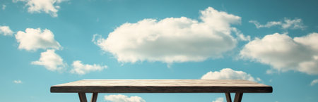 A serene wooden table stands alone against a vibrant blue sky dotted with fluffy white clouds. This peaceful scene evokes feelings of calm and simplicity, perfect for use in creative projects.の素材