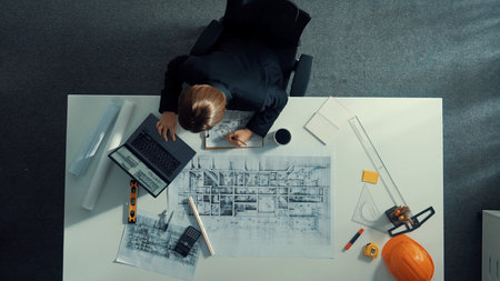 Top view of manager looking at blueprint while sitting at meeting table with project plan,...