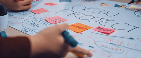 Hands of diverse individuals engage in a collaborative brainstorming session, utilizing sticky notes and markers on a large paper for project development ideas.の写真素材