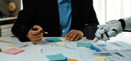 A business professional collaborates with a robotic arm while analyzing data charts and graphs,...