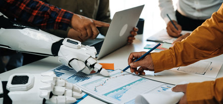 A diverse team collaborates in a modern workspace, utilizing a robotic arm alongside humans to...