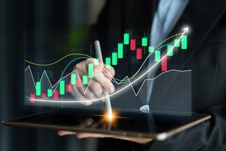 A business professional is using a tablet to analyze digital financial charts, highlighting...
