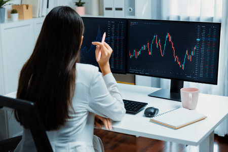 Young beautiful Asian businesswoman looking on pc to analyze profitable of exchange stock market...