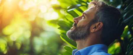 A contemplative man with a beard gazes upwards, surrounded by vibrant greenery and warm sunlight filtering through leaves, embodying serenity and self-reflection.の素材