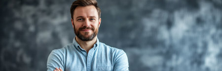 A confident young man with a beard stands against a textured gray background, showcasing a relaxed style. His friendly expression conveys approachability and professionalism.の素材