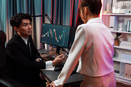 Asian businesswoman standing to discuss with dynamic stock exchange graph with partner to taking...