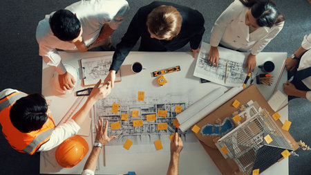 Top down view of skilled engineer team talking while looking at project plan. Aerial view of group...