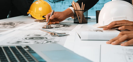 A focused team of engineers collaborates on detailed construction plans in an office environment,...
