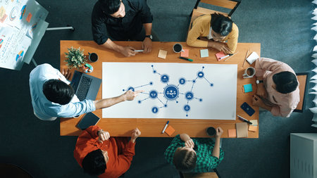 A diverse group of individuals engages in a brainstorming session over a large table, mapping out...