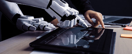 A human hand interacts with a robotic hand on a digital tablet, showcasing a collaboration between...