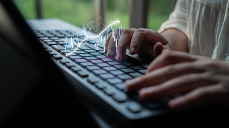 A woman engages with a laptop, typing while digital finance graphs illustrate upward growth,...
