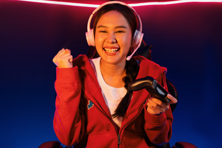 Host channel of smiling Asian girl streamer with joystick playing with raising fist up winning...