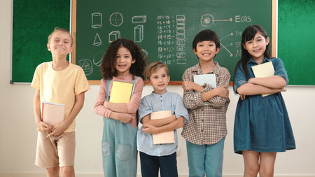 Multicultural elementary student in casual cloth looking at camera while standing at classroom....
